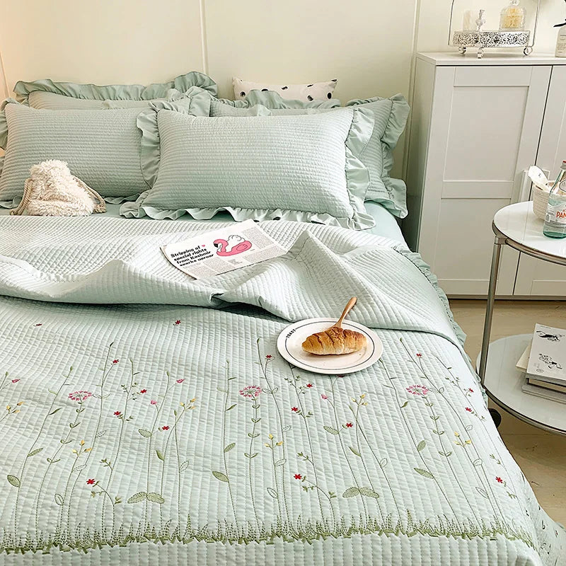 A light mint green floral embroidery quilt bedspread set displayed on a bed with white linens.