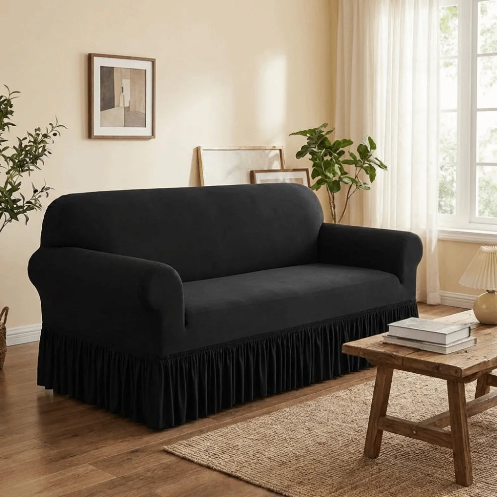 A black dustproof stretch sofa slipcover placed on a wooden floor with a rug and natural light.