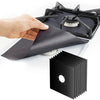A hand is placing a black reusable aluminum stove burner protector mat onto a stovetop grate.