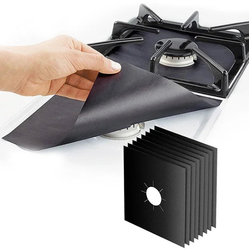 A hand is placing a black reusable aluminum stove burner protector mat onto a stovetop grate.