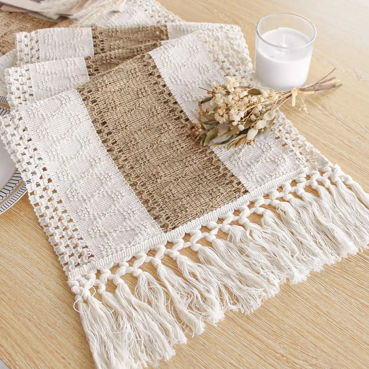 A beige and white boho linen cotton table runner with tassels rests on a wooden surface next to a glass of milk.