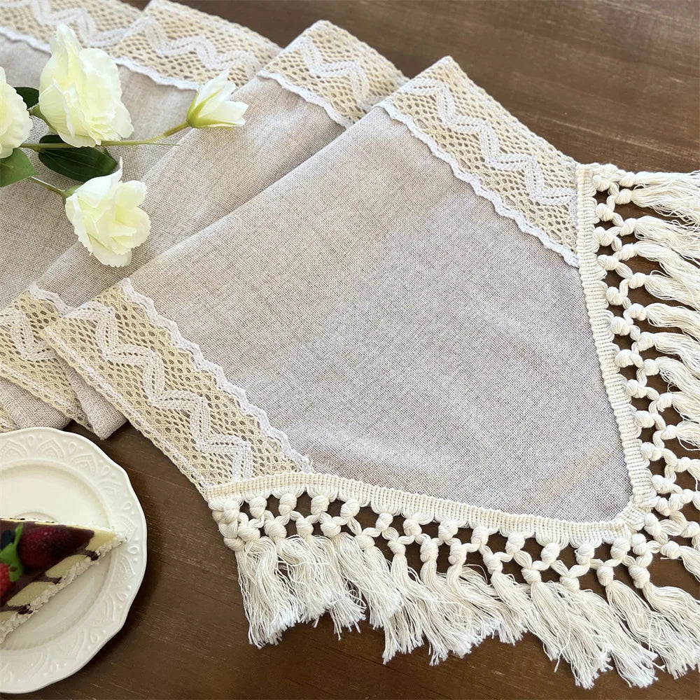 A beige crochet macrame lace table runner with fringed edges is displayed on a wooden surface.