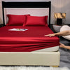 A luxurious red fitted sheet and pillow set displayed on a bed with a black headboard.