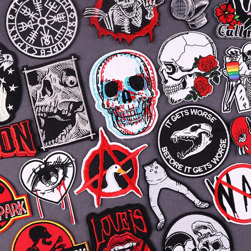 A collection of embroidered patches featuring skulls, roses, and various graphic designs on gray fabric.