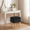 A dark gray faux fur ottoman with gold metal legs displayed on a white vanity table.