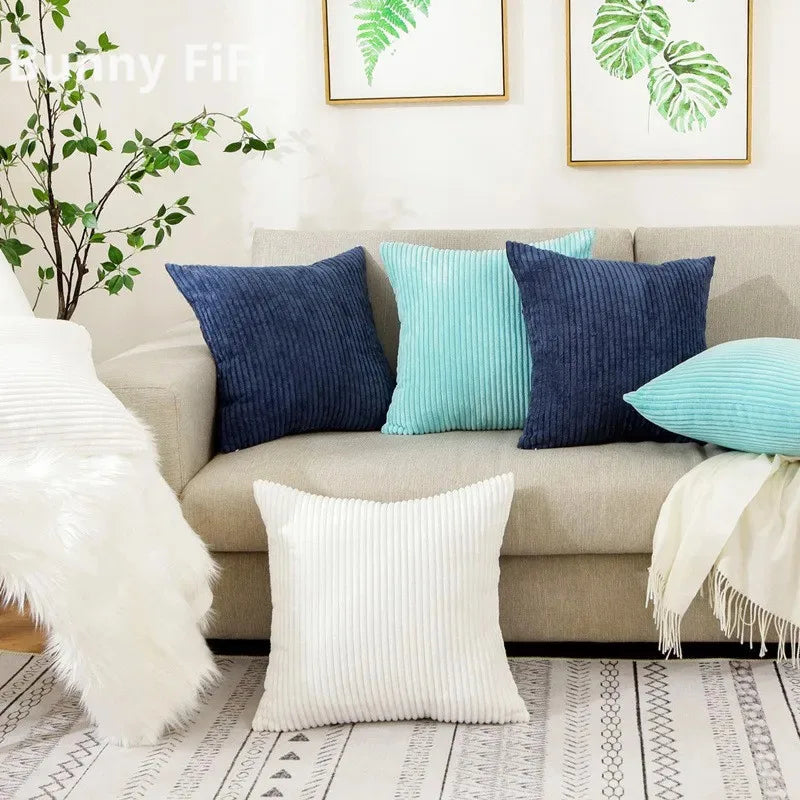 A collection of navy, teal, and white corduroy striped throw pillows displayed on a light sofa.