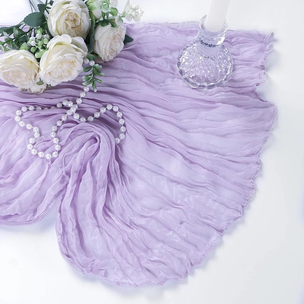 A lilac cheesecloth table runner with ruffled edges, adorned with white roses and pearl strands.