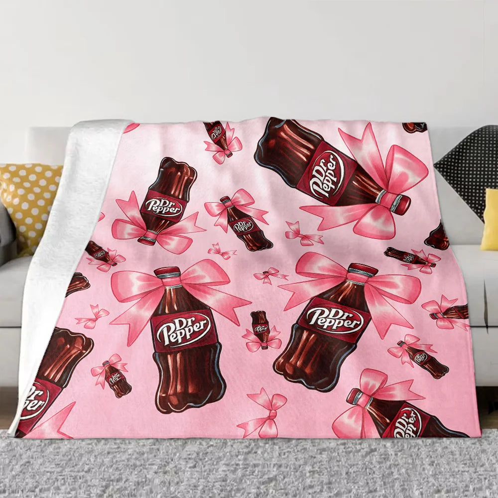 A pink cozy blanket featuring a repeating pattern of Dr. Pepper bottles with pink ribbons.