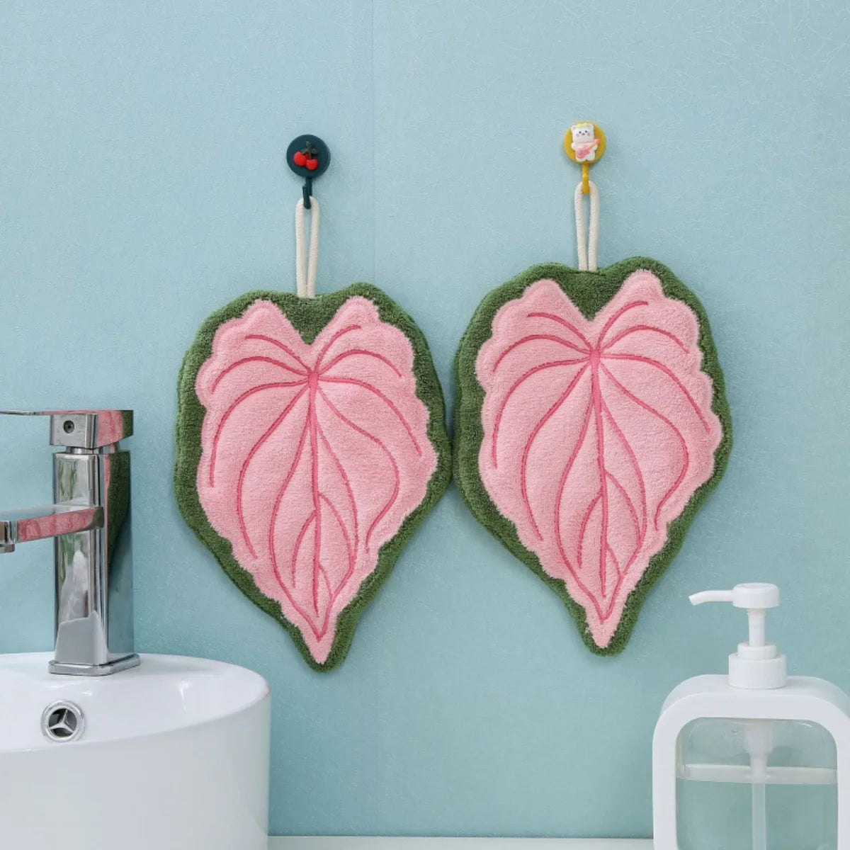 Two heart-shaped hand towels with pink and green leaves hanging on a light blue wall.
