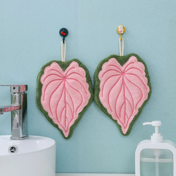 Two heart-shaped hand towels with pink and green leaves hanging on a light blue wall.
