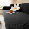 A dark gray textured sofa cover featuring a white flower cushion and an orange glass on a light-colored sofa.