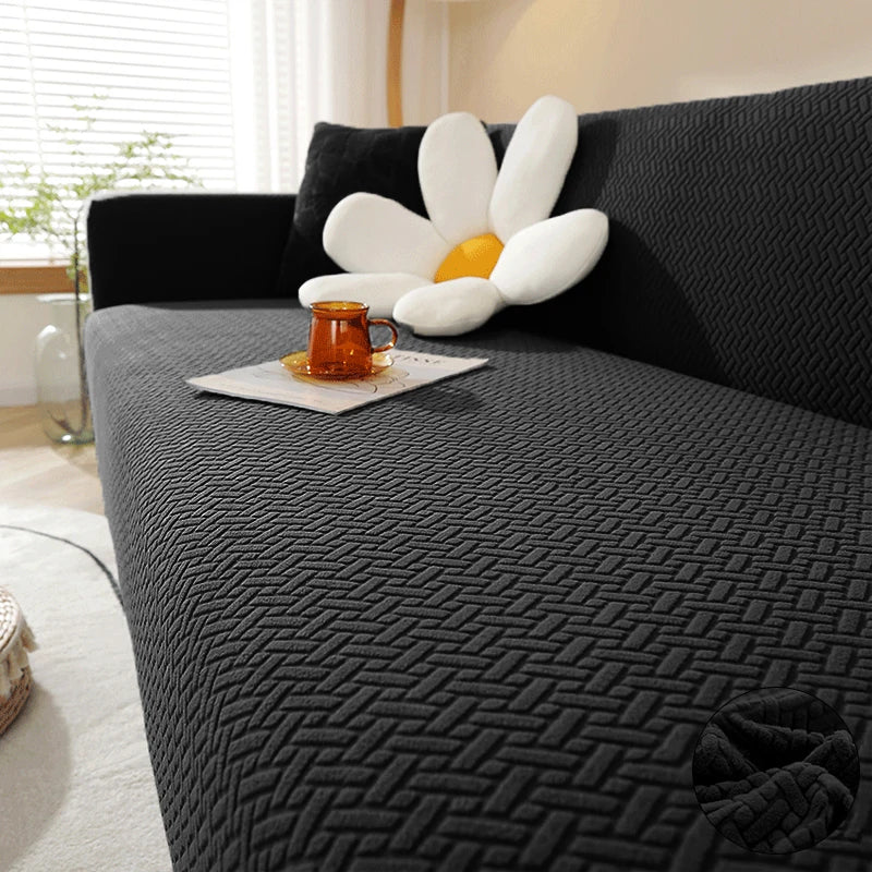 A dark gray textured sofa cover featuring a white flower cushion and an orange glass on a light-colored sofa.