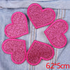 Five pink glitter heart shaped iron-on patches laid out on a denim fabric background.