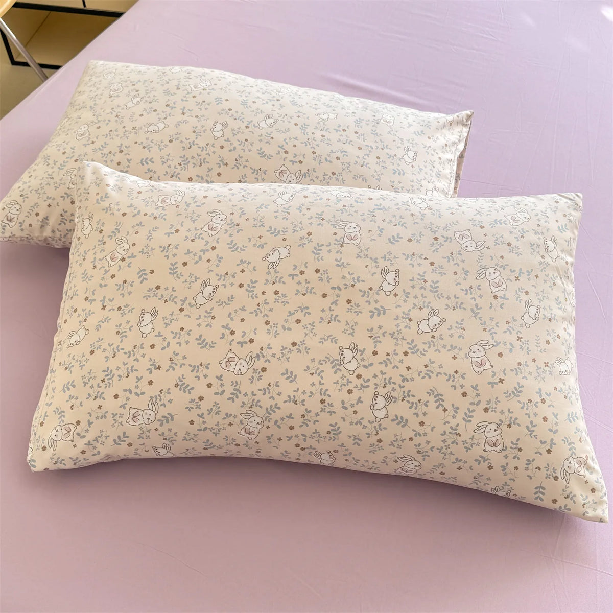 A pair of light beige floral printed pillow covers resting on a purple surface.