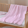 A pink large 6-layer cotton gauze blanket draped over a wooden crib mattress.