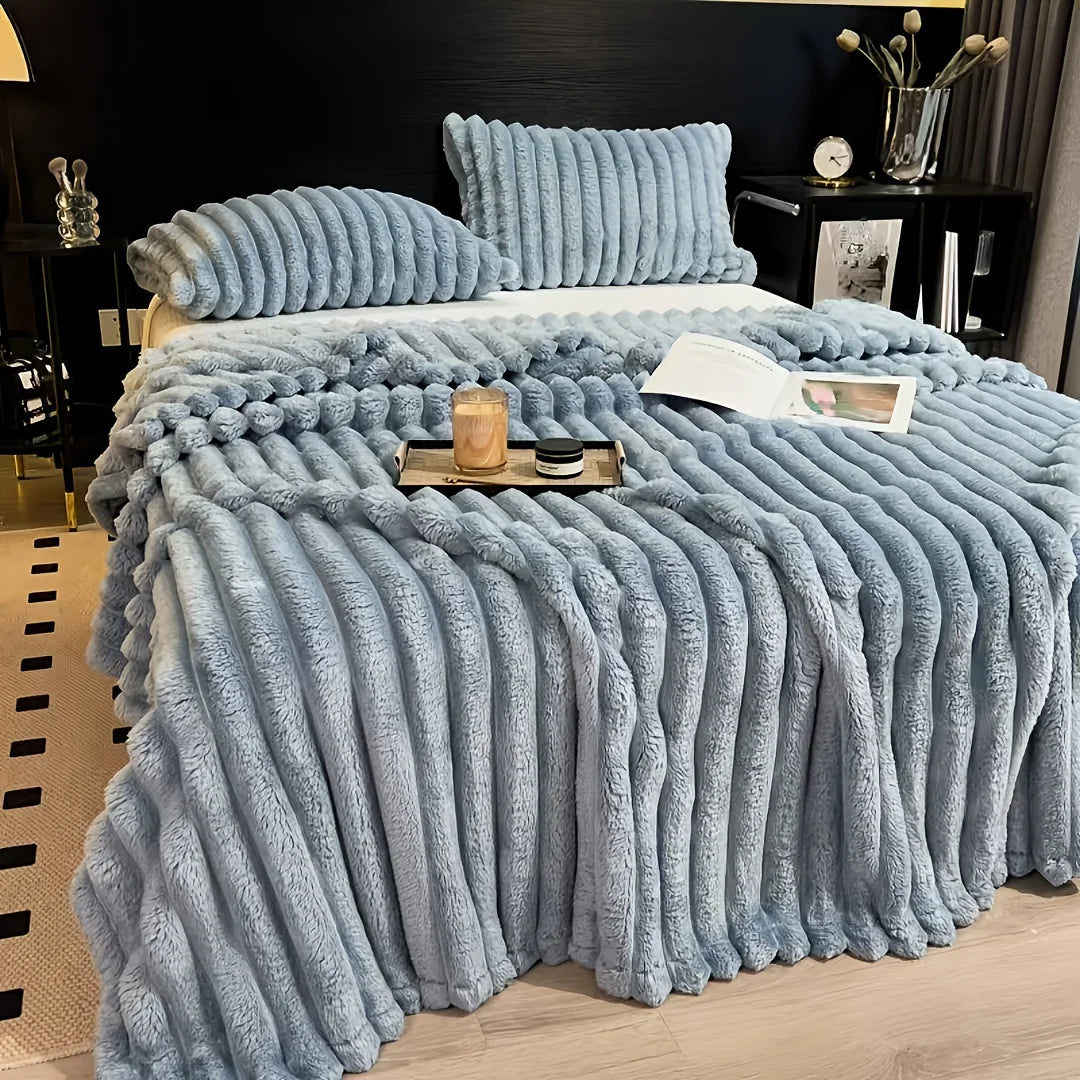 A light blue fluffy blanket with vertical stripes is draped over a bed, featuring a textured, soft appearance.