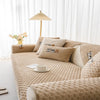 A beige plush sofa cover with decorative pillows and a light-colored floor lamp in a bright room.