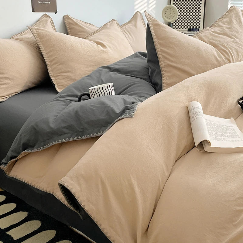 A close-up of a beige and gray luxurious washed cotton bed linen set featuring pillows and a duvet on a dark bed.