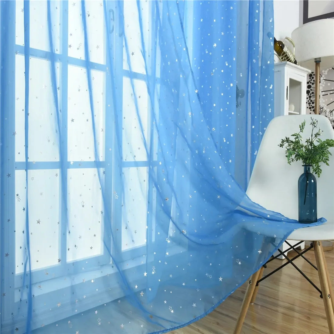 Light blue tulle curtains with silver stars draped over a window.
