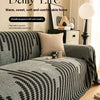 A gray chenille sofa cover with black herringbone pattern and tassel fringes displayed on a sofa.