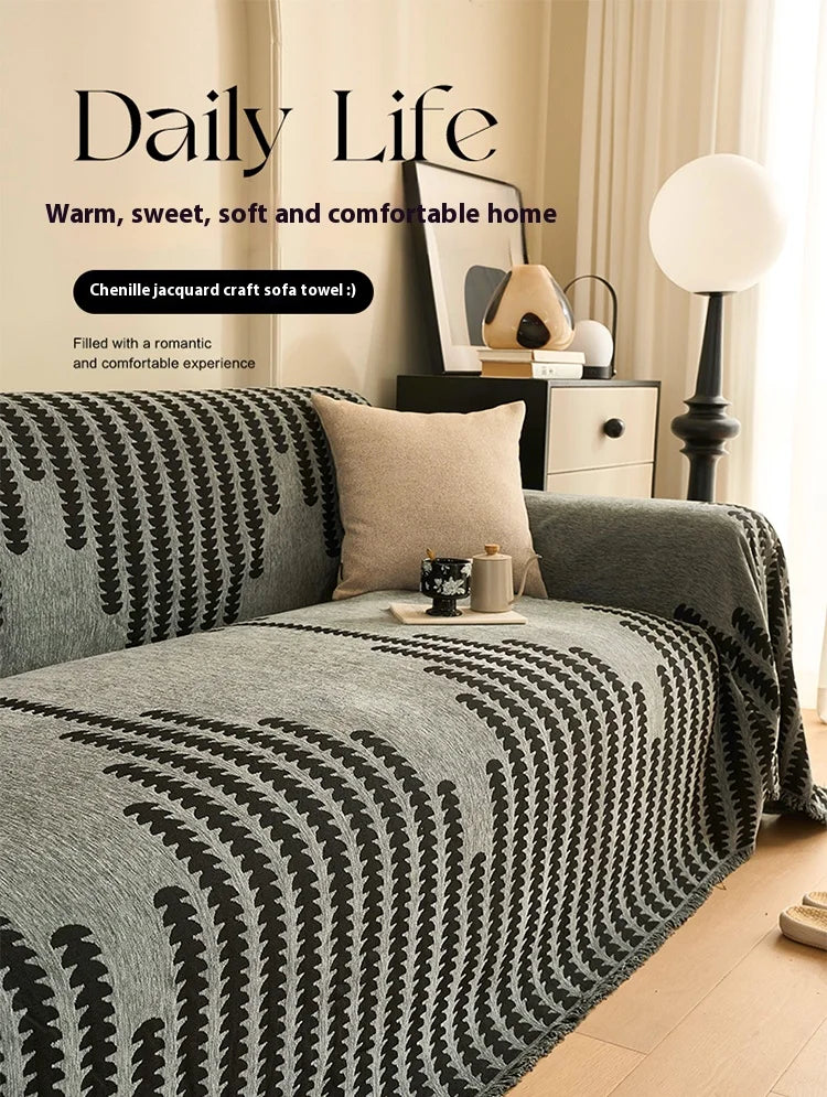 A gray chenille sofa cover with black herringbone pattern and tassel fringes displayed on a sofa.