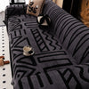 A close-up of a gray knitted sofa protector featuring a black geometric pattern and decorative pillows.