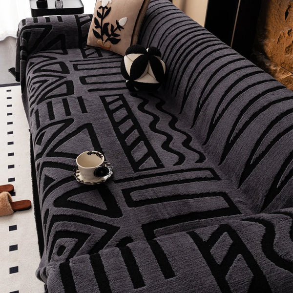 A close-up of a gray knitted sofa protector featuring a black geometric pattern and decorative pillows.