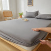 A close-up of a gray fitted sheet being handled on a wooden bed frame.