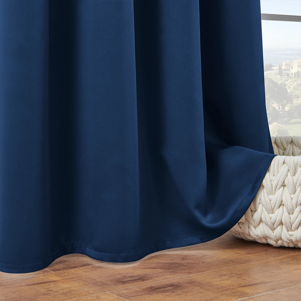 A dark navy blue blackout window curtain draped next to a window with a view of green hills.