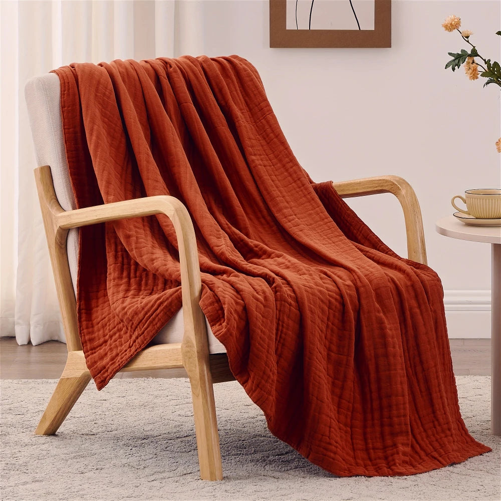 A terracotta orange woven blanket draped over a light wooden chair.