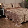 A leopard print satin bed sheet set spread across a bed with neutral tones and green foliage in the background.