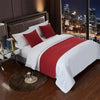 A white bed with red accent pillows and a red blanket, set against a dark room backdrop.