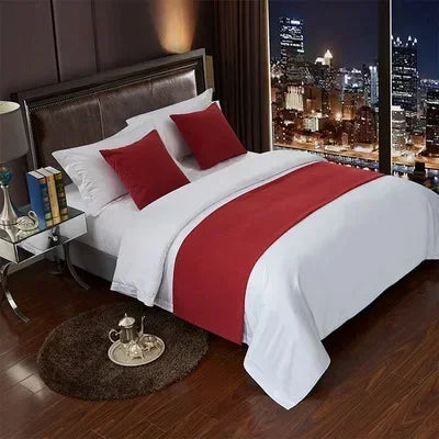 A white bed with red accent pillows and a red blanket, set against a dark room backdrop.