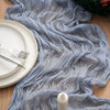 A gray crinkled cheesecloth table runner draped over a wooden surface with plates and a pine wreath.