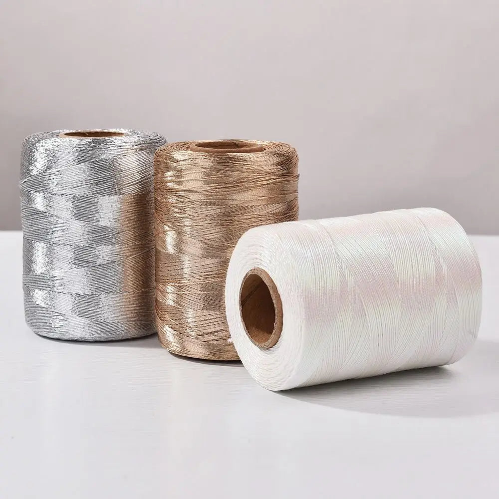 Three spools of glitter metallic yarn in silver, gold, and white are displayed on a white surface.