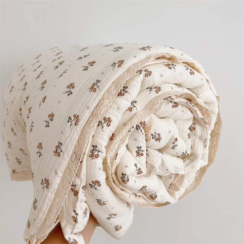 A rolled white muslin blanket with a floral print is shown against a light background.