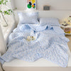 A light blue quilted quilt set with a white floral pattern displayed on a bed.
