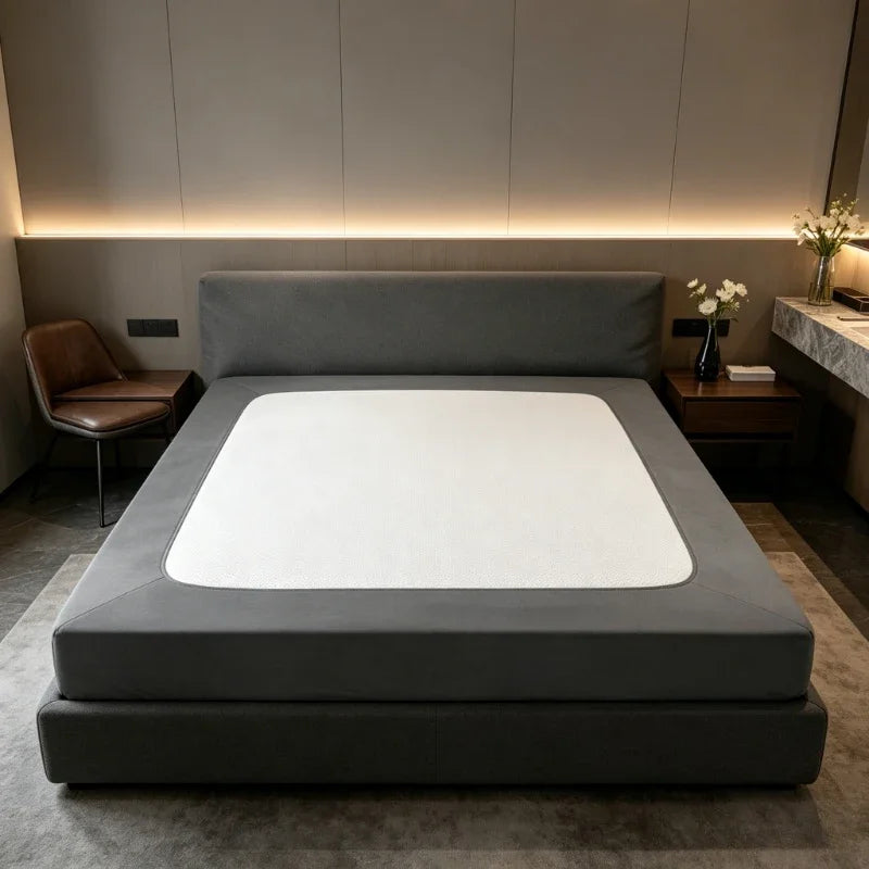A gray box spring protector cover is displayed on a bed, featuring a white insert and modern lighting.