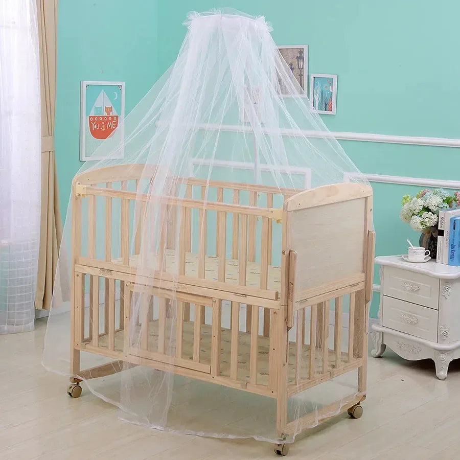 A light wood crib draped with a sheer white mosquito net for baby safety.