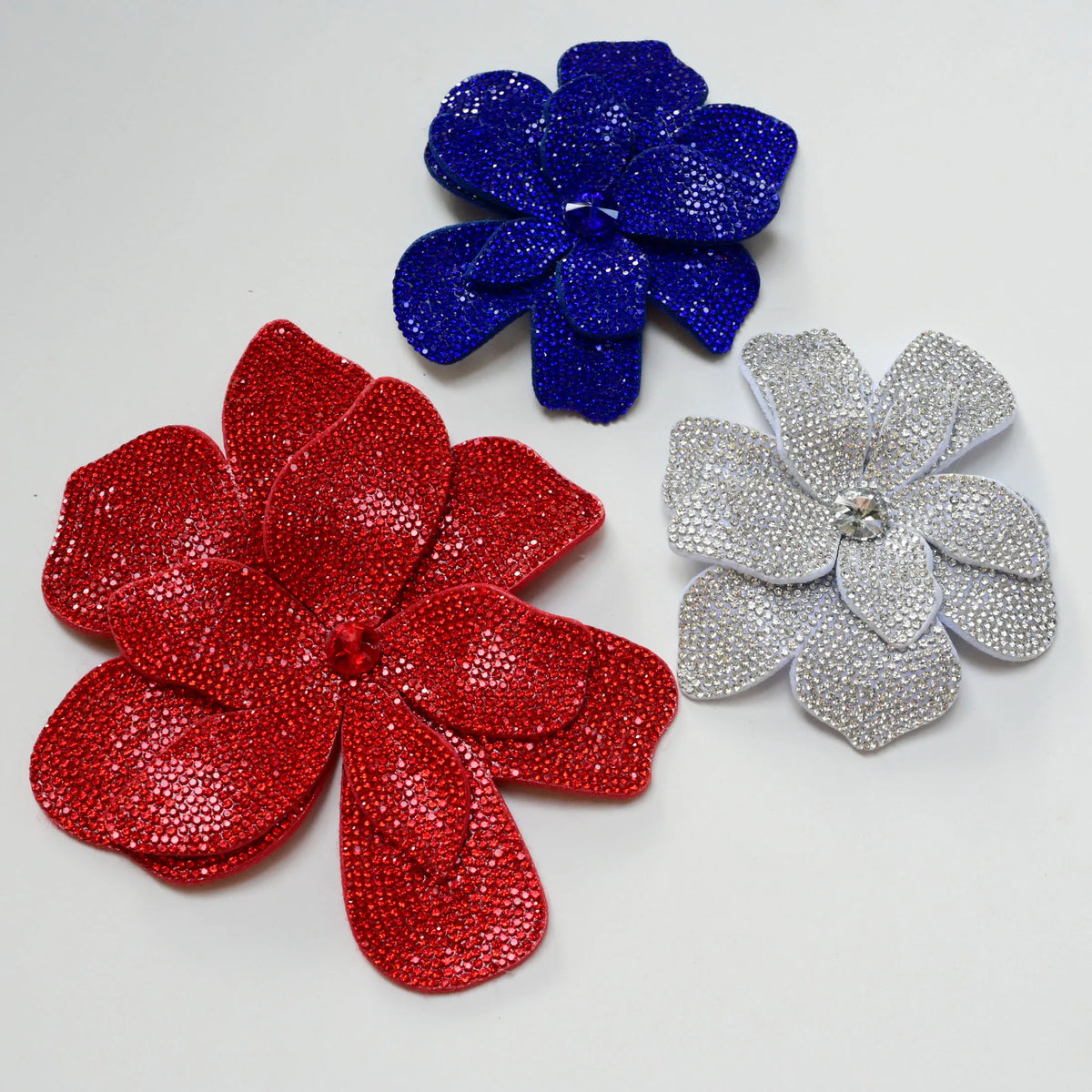 Three rhinestone flower applique patches in blue, red, and silver are displayed on a white background.