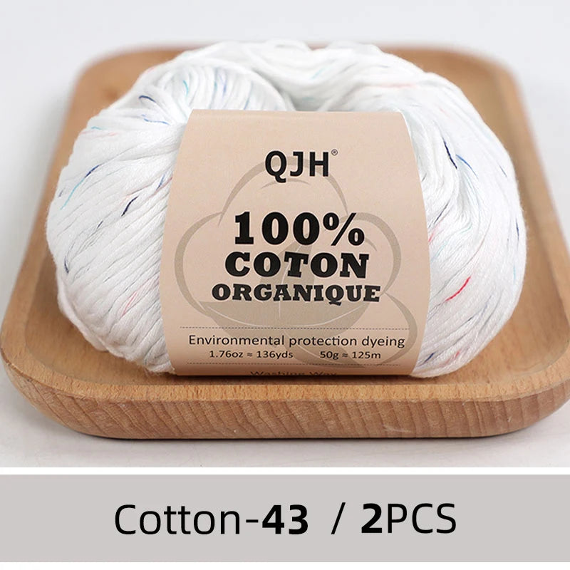 A ball of white organic cotton yarn labeled QJH 100% COTON ORANIQUE resting on a wooden board.