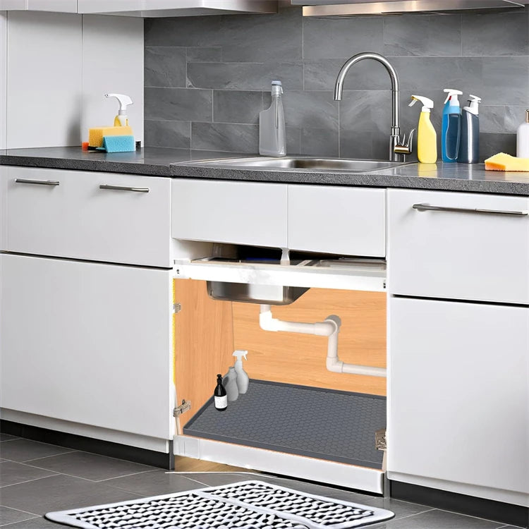 A kitchen sink area showing a stainless steel sink, faucet, and white cabinetry with a silicone drain mat visible inside the 