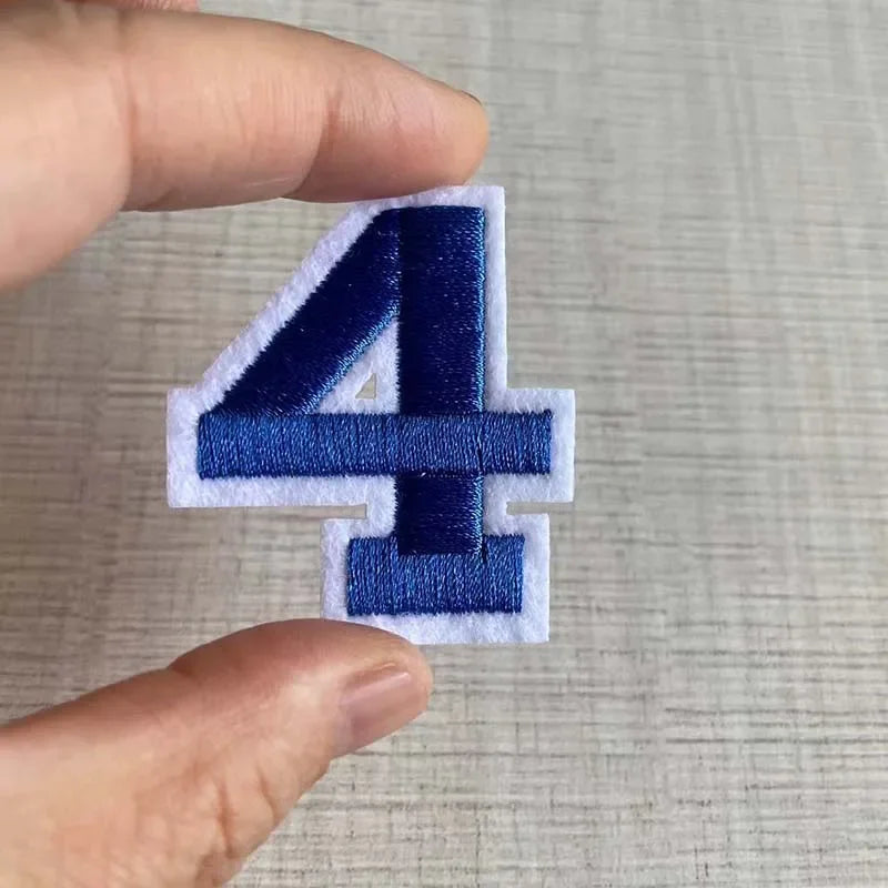 A hand holds a navy blue embroidered number 4 patch on a light surface.