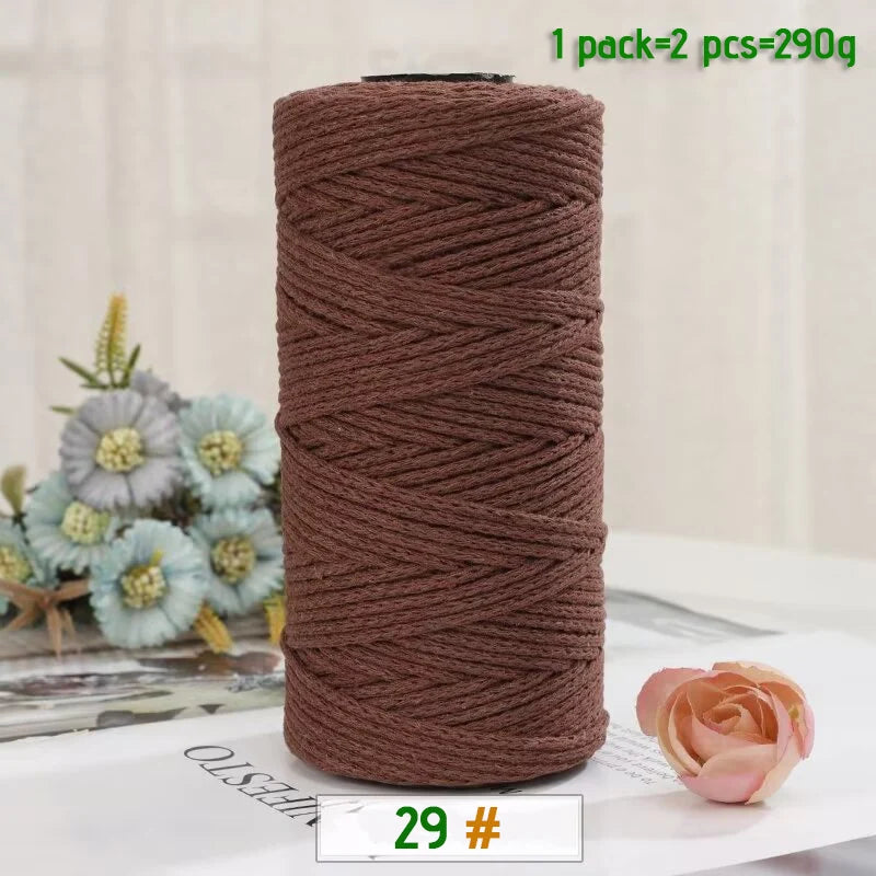 A roll of medium-thick brown hand-woven cotton yarn for crafting, next to a pink rose flower.