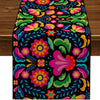 A vibrant floral pattern on a black linen table runner featuring pink, purple, orange, and green leaves.