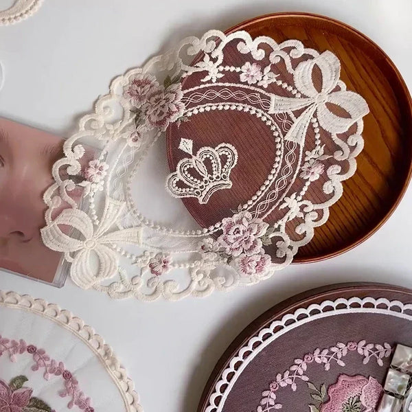 A set of elegant oval lace embroidered coasters featuring pink floral patterns on dark brown wood.