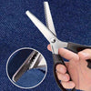 A hand holds a pair of stainless steel serrated edge fabric scissors against a dark blue fabric background.