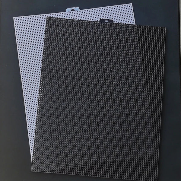 Two black and white plastic grids for cross stitching displayed against a dark background.