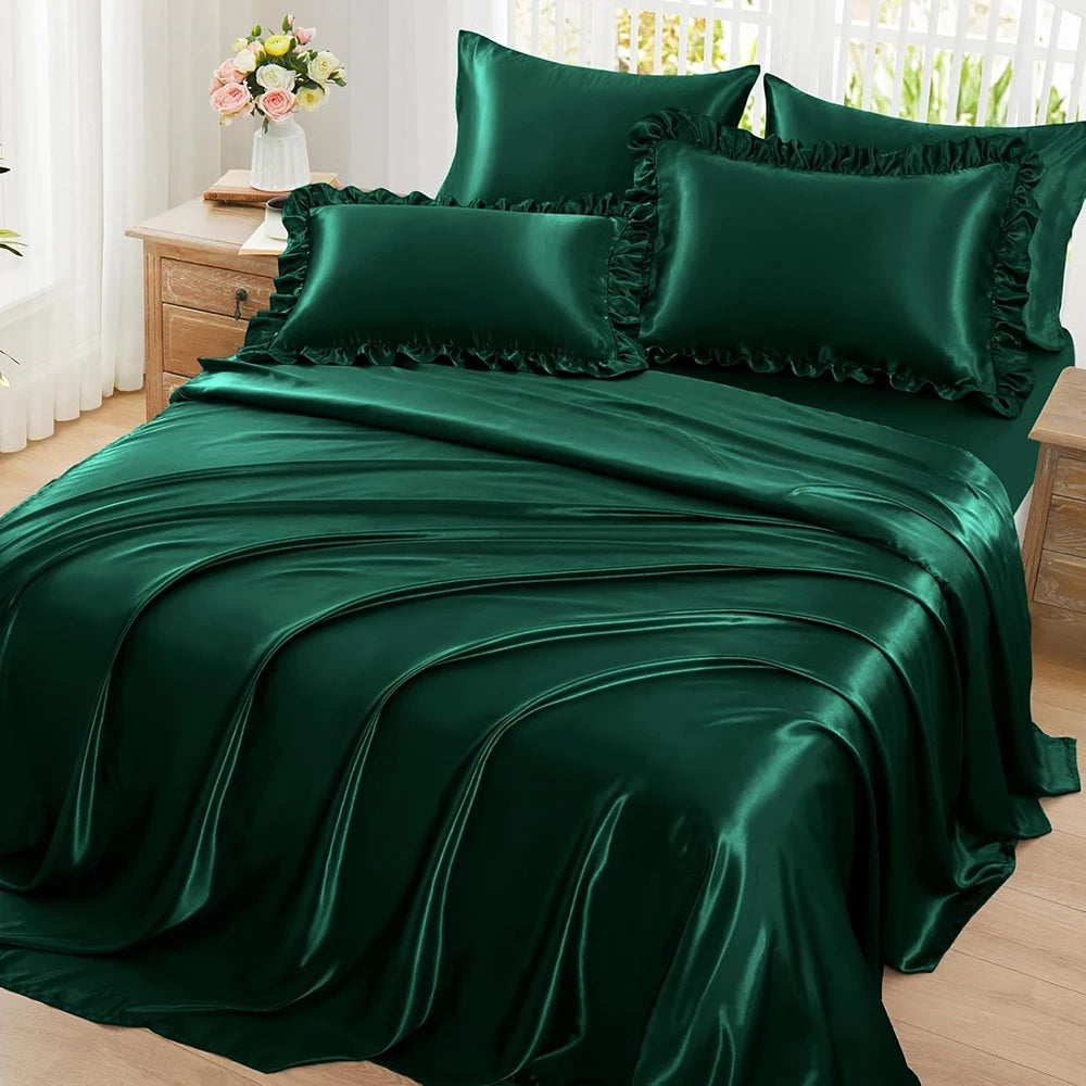 A set of two emerald green ruffled satin pillowcases with silky envelope closures displayed on a bed.