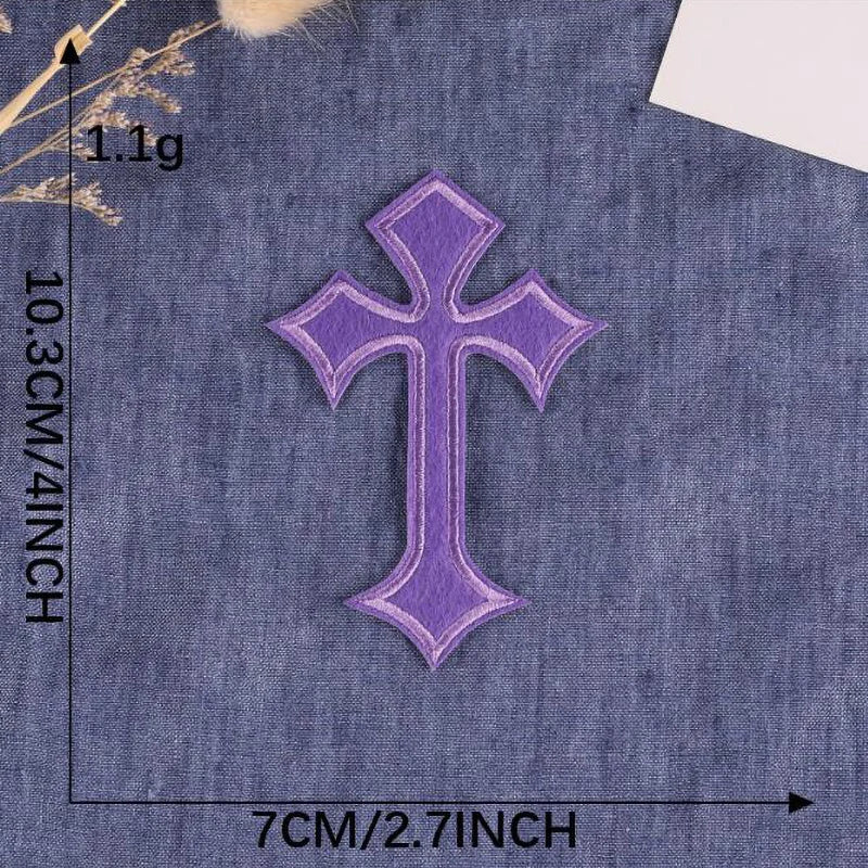 A purple cross embroidery patch on a denim fabric background.